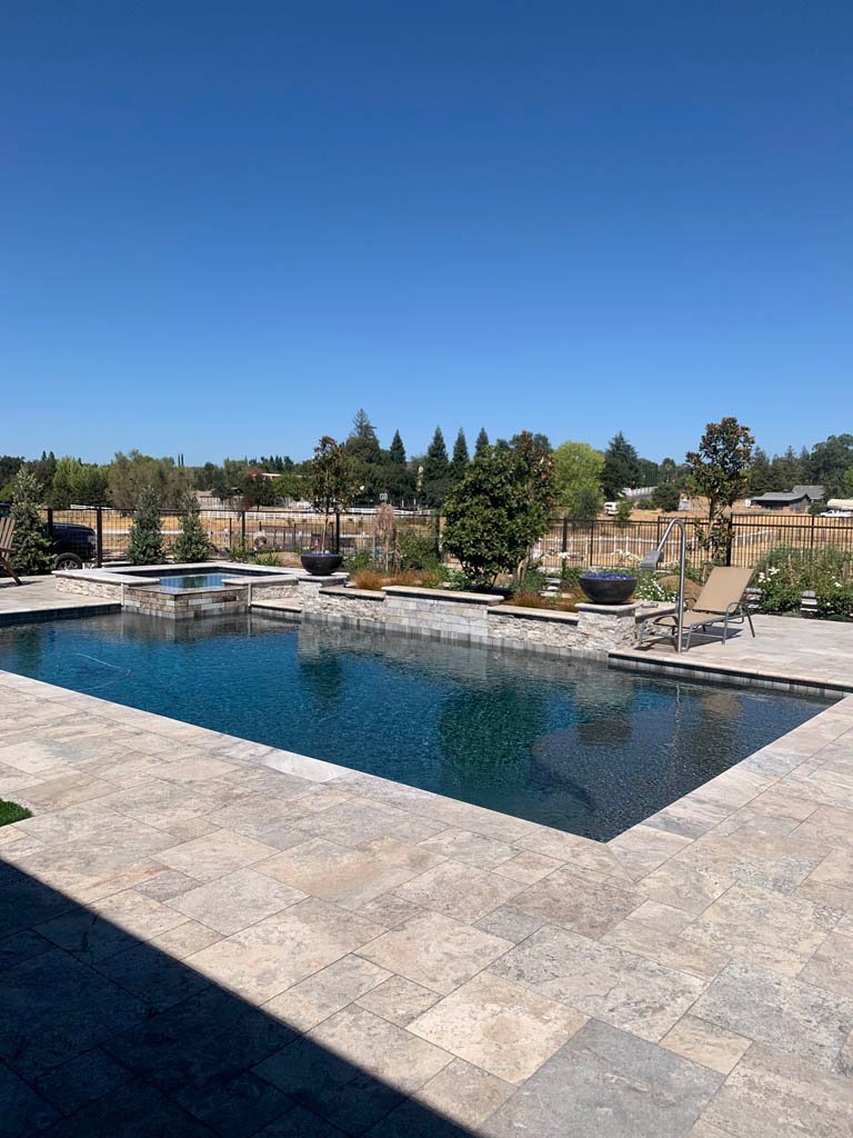 Outdoor swimming pool with stone deck and scenic trees backdrop.