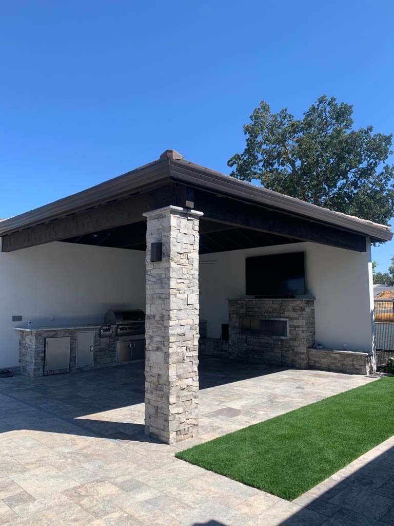 Outdoor kitchen pavilion with stone columns and modern appliances.