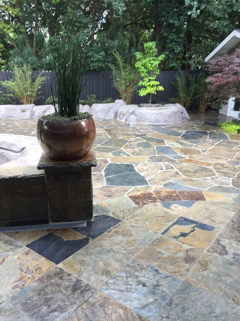 Stone patio with plant in ceramic pot and landscaped garden.