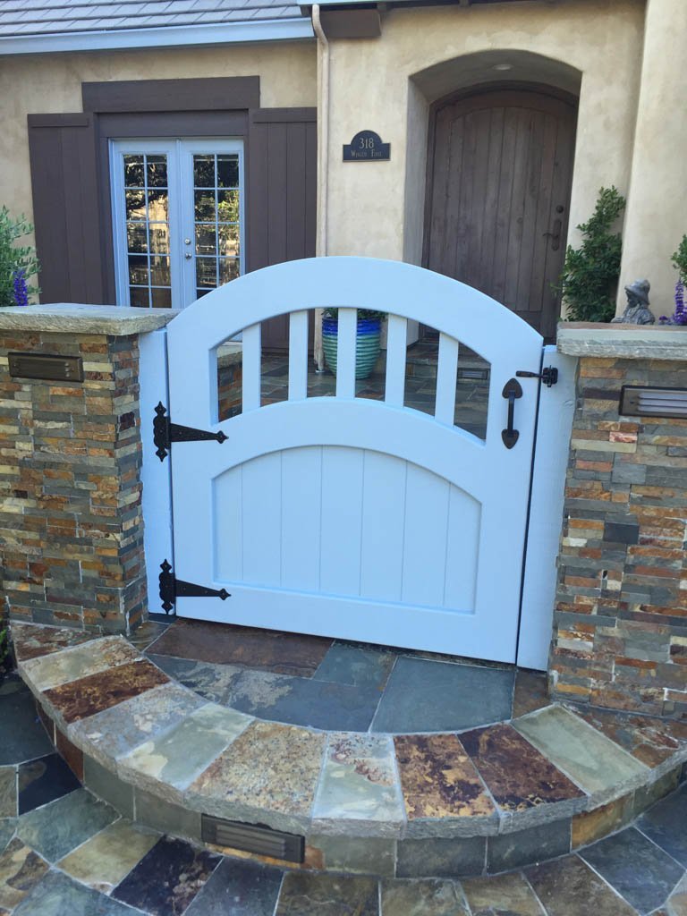 Arched white gate at stone-walled home entrance.