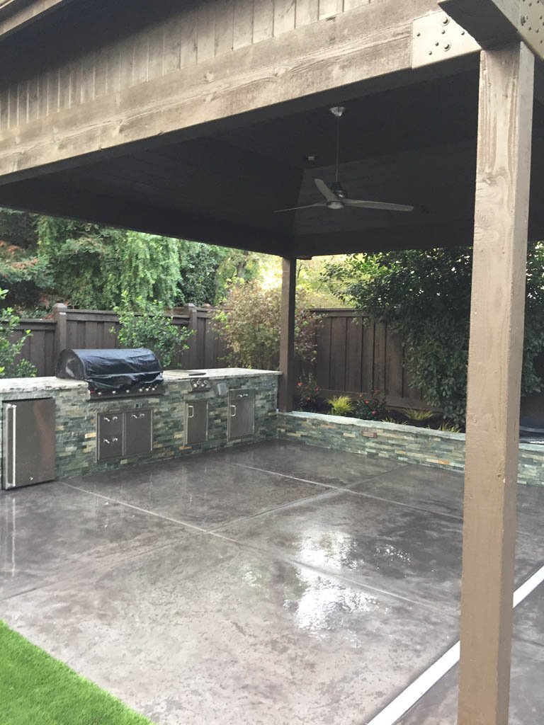 Outdoor kitchen patio with ceiling fan and stone counters.