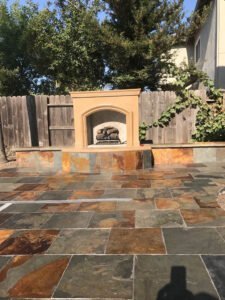 Outdoor patio with stone flooring and built-in fireplace.