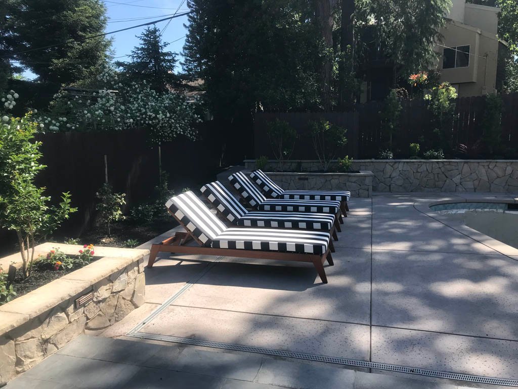 Sunny backyard with striped loungers by pool.