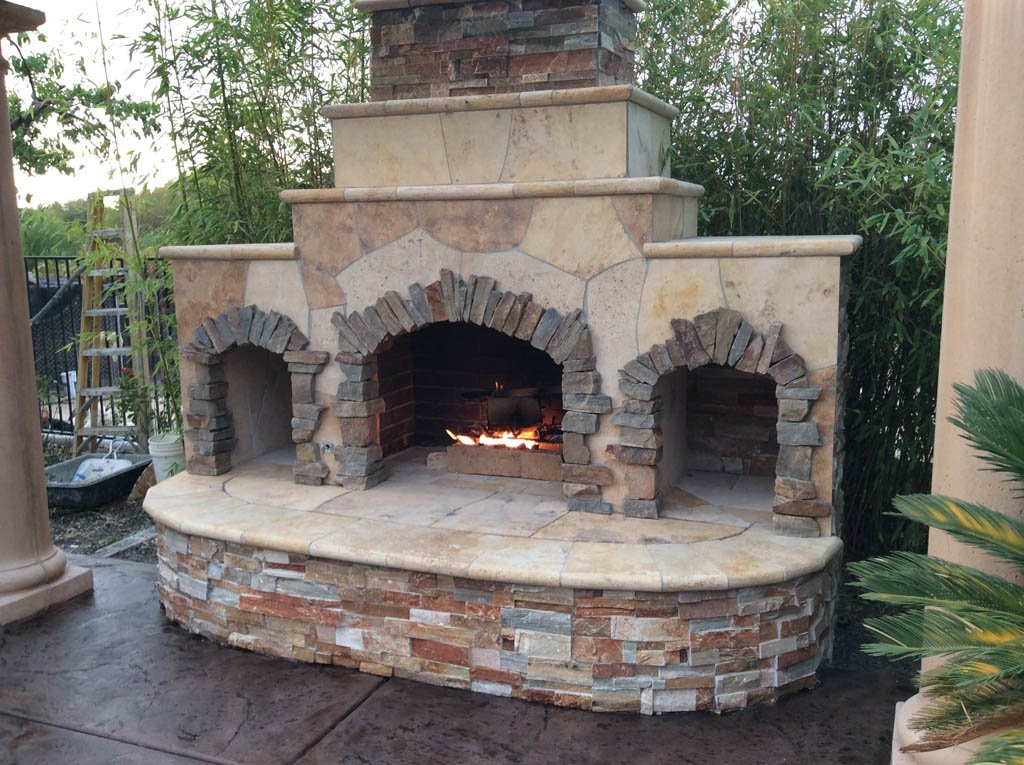 Outdoor stone fireplace with lit fire and arches.