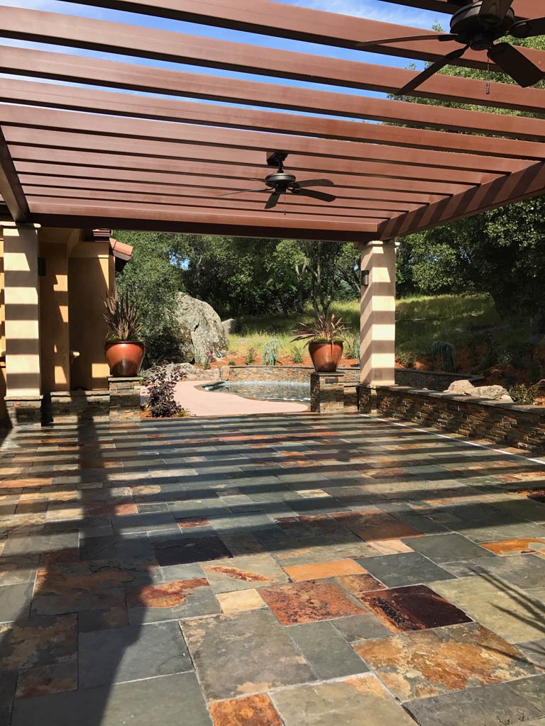 Pergola-covered patio with tiled floor and landscape view.