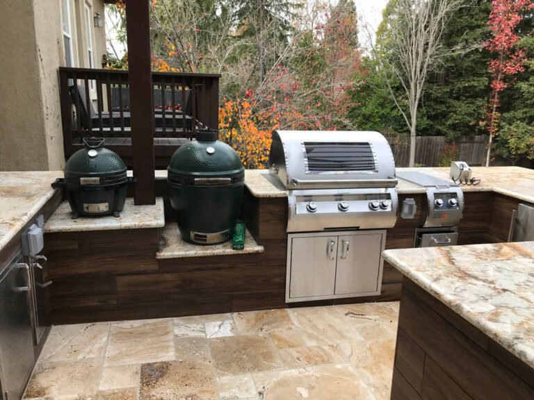 Outdoor kitchen with grills and autumn trees in background.