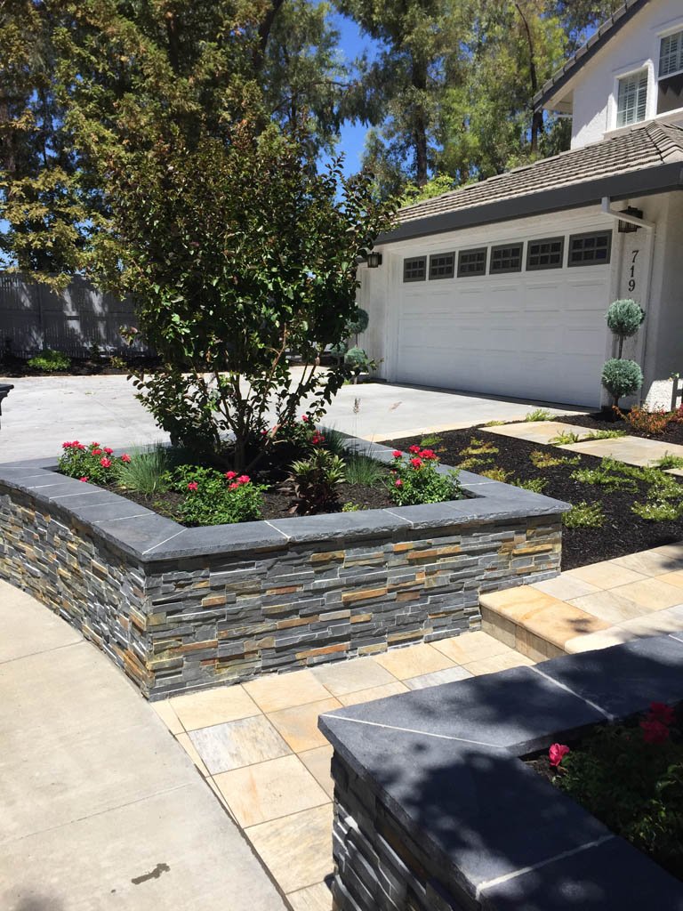 Landscaped front yard with stone walls and driveway.