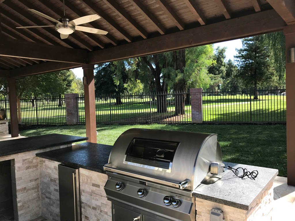 Outdoor kitchen with grill under covered patio overlooking park.