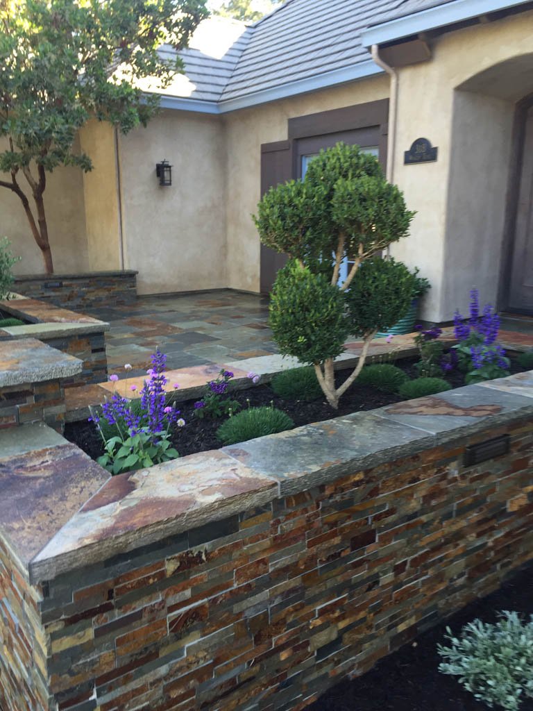 Elegant courtyard with topiary and stone wall landscaping.