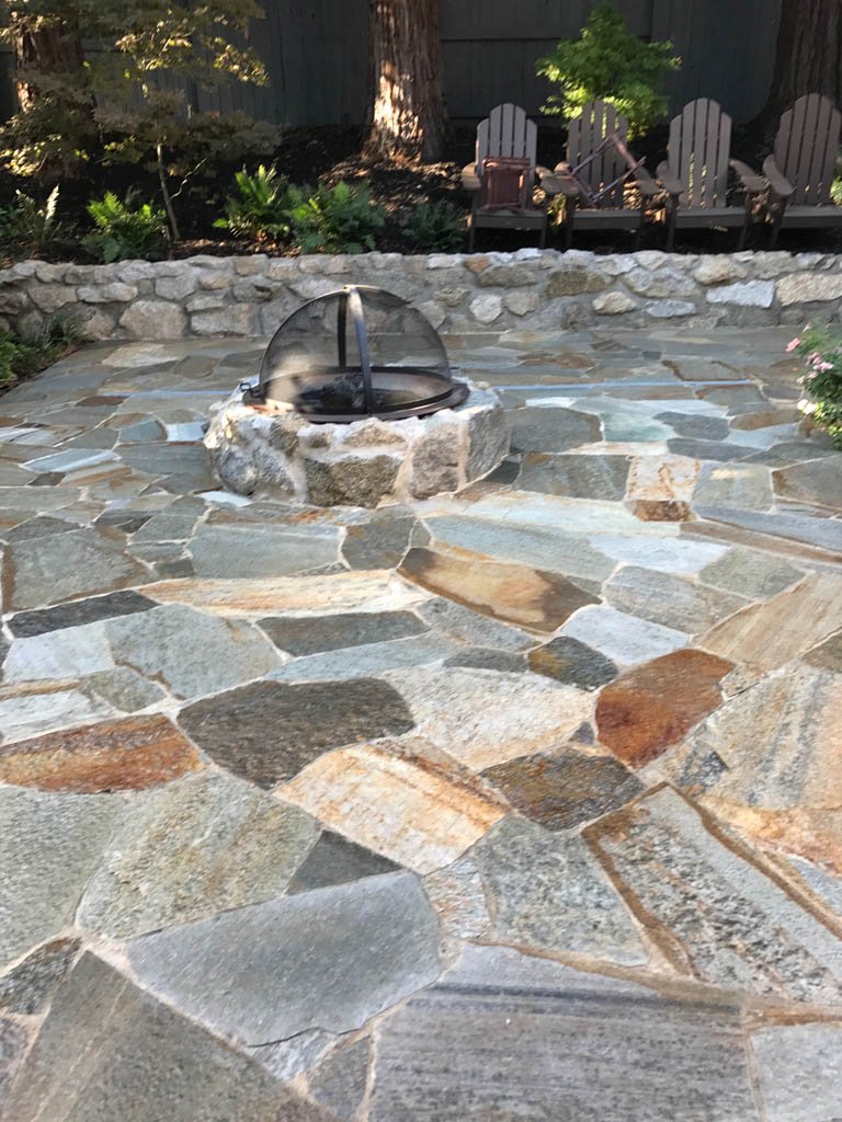 Stone patio with fire pit and wooden chairs.