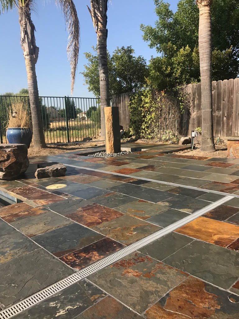 Slate-tiled patio with palm trees and wooden fence.