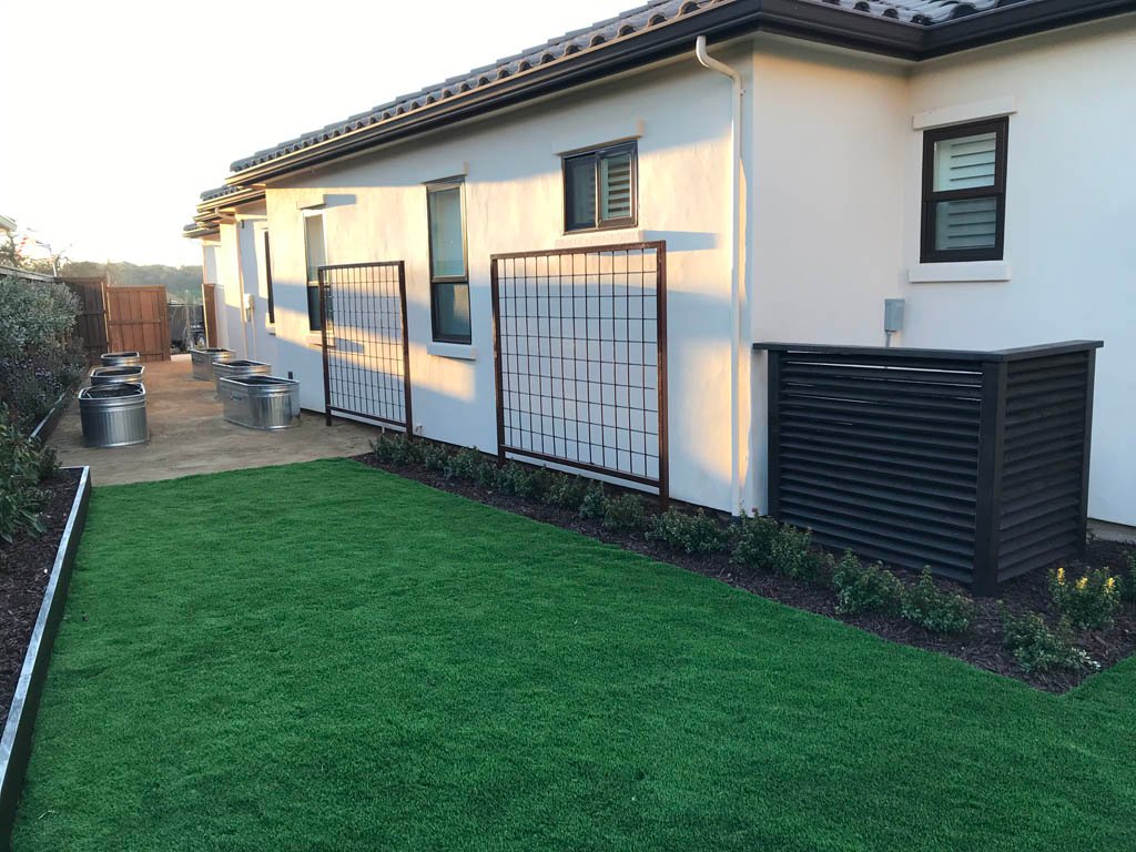 Modern house exterior with manicured lawn and privacy screens.