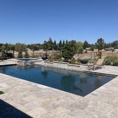 Outdoor swimming pool with stone deck and scenic trees backdrop.