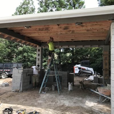 Workers constructing a carport with cinder blocks and wood.