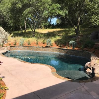 Outdoor pool with natural stone edge surrounded by trees.