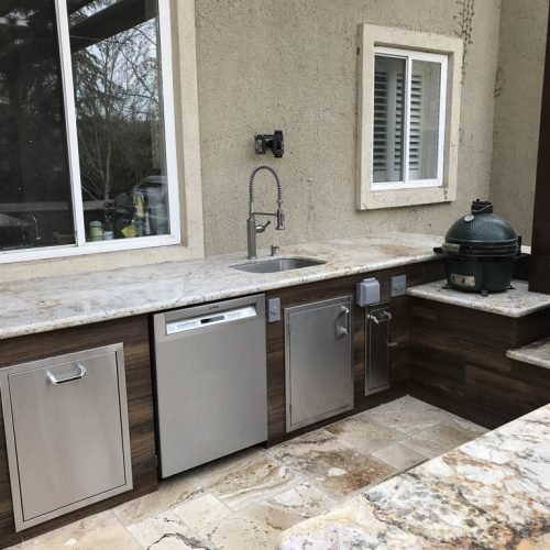 Outdoor kitchen with sink, dishwasher, and dual grills.