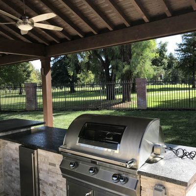 Outdoor kitchen with grill under covered patio overlooking park.