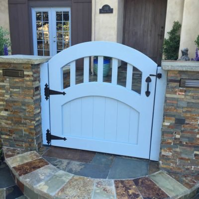 Arched white gate at stone-walled home entrance.