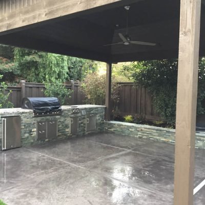 Outdoor kitchen patio with ceiling fan and stone counters.