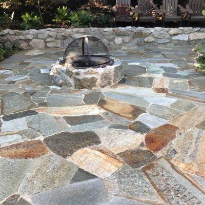 Stone patio with fire pit and wooden chairs.