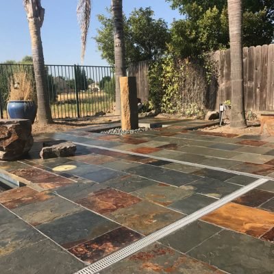 Slate-tiled patio with palm trees and wooden fence.