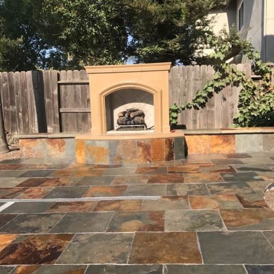 Outdoor patio with stone flooring and built-in fireplace.