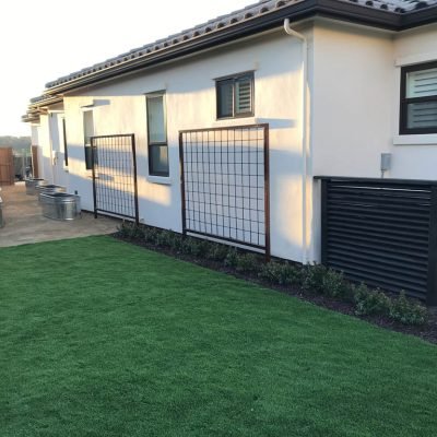 Modern house exterior with manicured lawn and privacy screens.