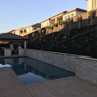 Outdoor pool with cabana and hillside homes at sunset.