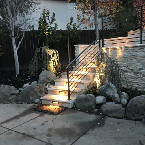 Illuminated garden staircase with stone details at dusk.