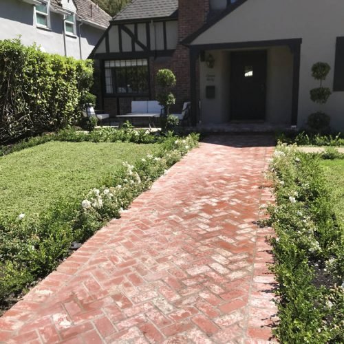 Brick path leading to Tudor-style house with green lawn.